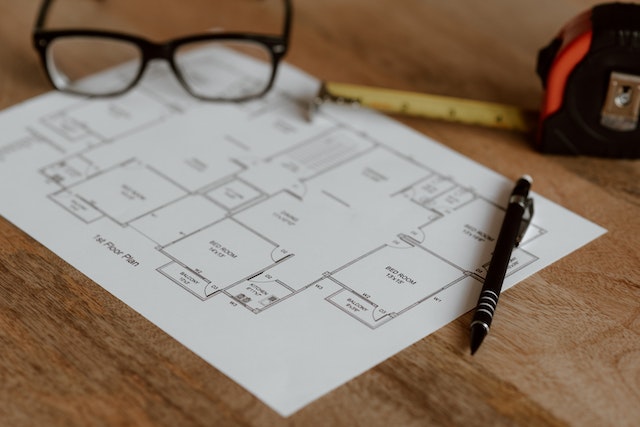 a floor plan next to glasses, a measuring tape, and pen